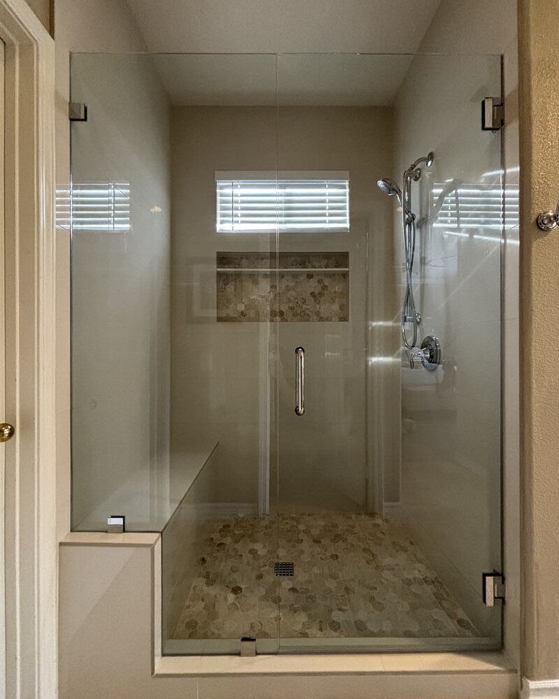 Frameless shower door with panel notched for a bench in San Marcos, CA